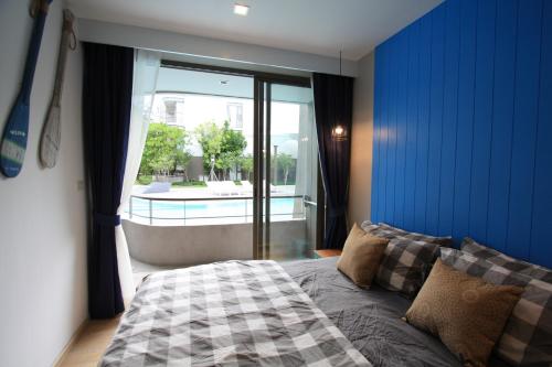 een slaapkamer met een blauwe muur, een bed en een raam bij บ้านแสนคราม หัวหิน Family Room - Pool Access ห้องติดสระ in Phetchaburi