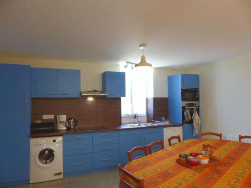 une cuisine avec des armoires bleues et une table avec une nappe dans l'établissement Gîte paisible face à l'église, idéal pour familles et amis, équipé tout confort, près de la nature - FR-1-489-416, à Fourilles