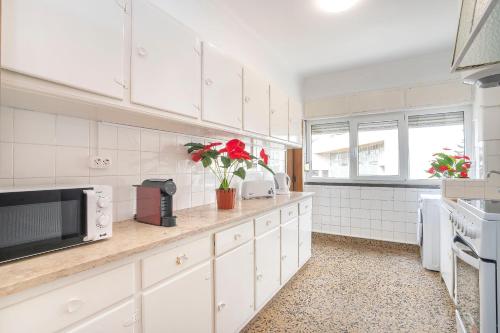 a kitchen with white cabinets and red flowers on the counter at Happy Holiday Cascais - Home in Cascais