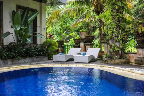 a pool with two lounge chairs next to a house at Amoya Inn in Ubud