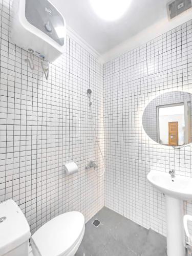 a white tiled bathroom with a toilet and a sink at OsOs Paviliun in Timuran