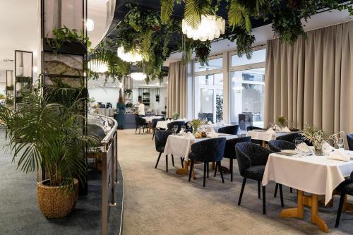 um restaurante com mesas brancas, cadeiras e plantas em Hotel Astor em Jastrzebia Gora