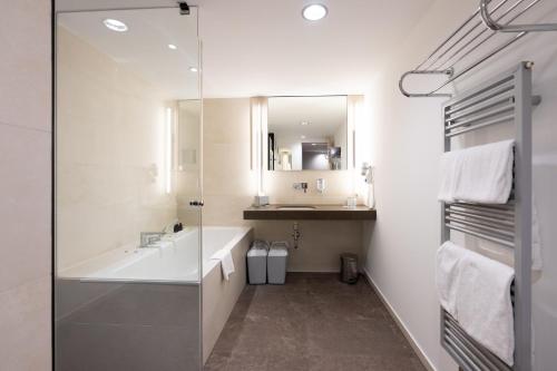 a bathroom with a tub and a sink and a mirror at Kongresshotel Potsdam am Templiner See in Potsdam