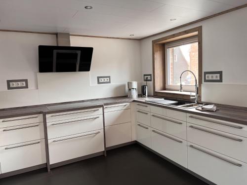 a kitchen with white cabinets and a tv on the wall at Dill Apartments Gadenstedt in Ilsede