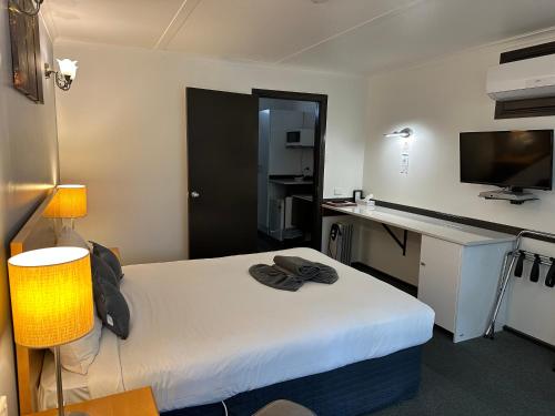 Habitación de hotel con cama, escritorio y TV. en Statesman Motor Inn, en Ararat