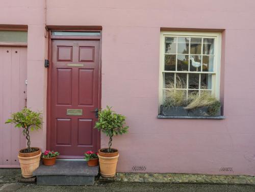 a pink house with a red door and potted plants at Seagull Cottage in Beaumaris