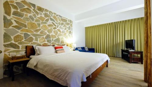 1 dormitorio con 1 cama grande y pared de piedra en Shire Homestay en Luodong