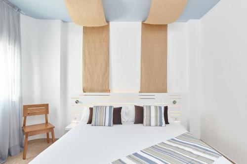 a bedroom with a white bed and a chair at Apartamentos Castaví in Es Pujols