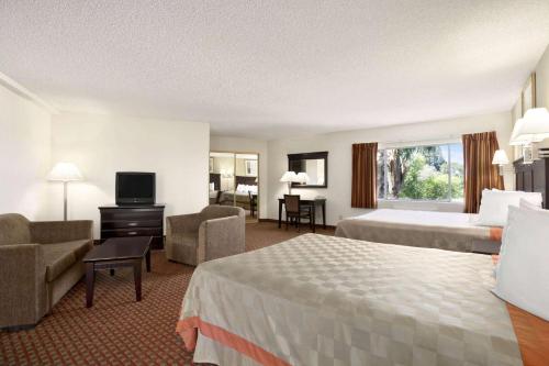 a hotel room with two beds and a couch and a television at Days Inn & Suites by Wyndham Rancho Cordova in Rancho Cordova