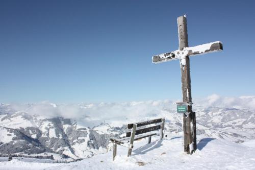 a cross on top of a snowy mountain with a bench at Hotel Garni Wieshof in Kirchberg in Tirol