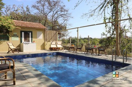 a swimming pool in a yard with chairs and a table at Asiatic Lion Lodge in Sasan Gir