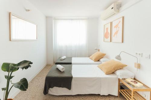a white bedroom with two beds and a plant at Casa Jam Barcelona in Barcelona