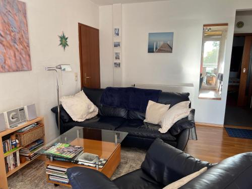 a living room with a black leather couch and a glass table at Ferienwohnung Christel in Wasserburg am Bodensee