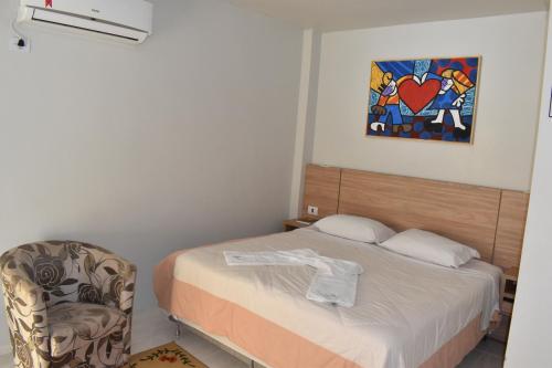 ein Schlafzimmer mit einem Bett, einem Stuhl und einem Gemälde in der Unterkunft Rai Hotel - By UP Hotel - próximo a Prefeitura in Cascavel