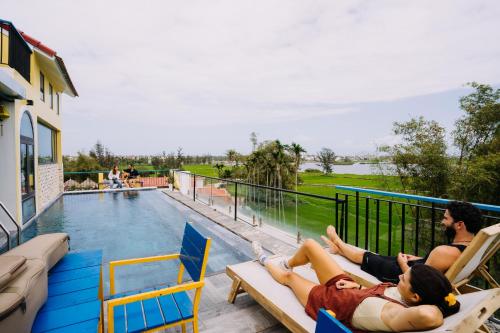two people laying on chairs next to a swimming pool at The Cuckoo's Nest Hostel and Bar managed by Hoianese in Hoi An