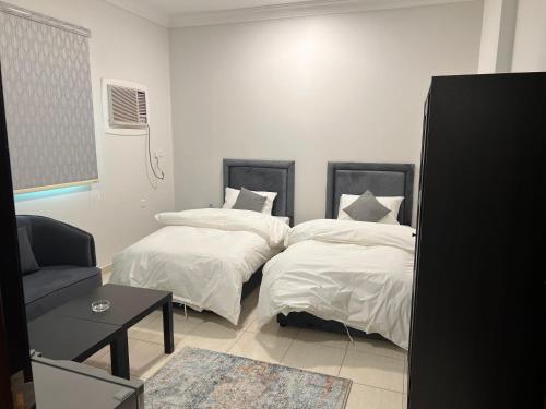 1 dormitorio con 2 camas con sábanas blancas y mesa en الشقق الذكية en Yanbu