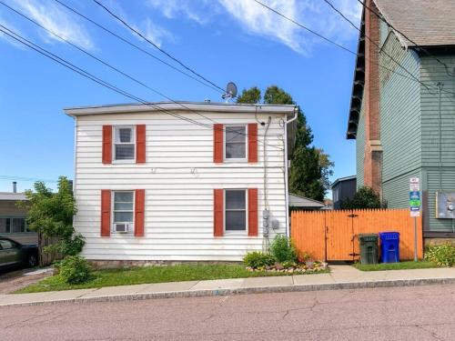a white house with orange shutters on a street at Bohemian Bungalow with Hot Tub in Winooski