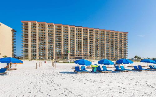 a beach with chairs and blue umbrellas and a hotel at Two-Bedroom Apartment in Orange Beach