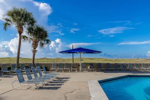 a pool with chairs and a blue umbrella and palm trees at One-Bedroom Apartment in Orange Beach