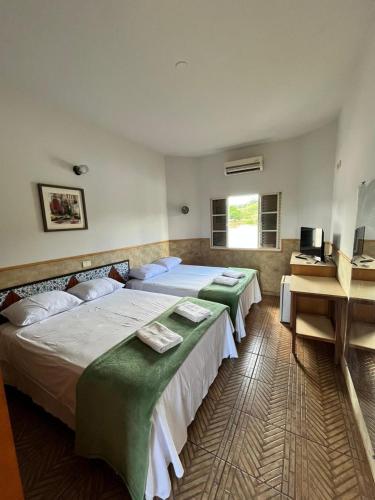 a bedroom with two beds and a desk and a window at Hotel Fazenda Pousada da Serra in Goianésia