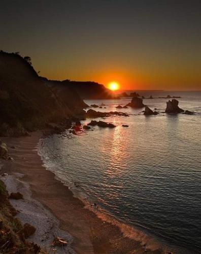a sunset over a beach with the sun setting at Hotel Restaurante el Fornon in Novellana