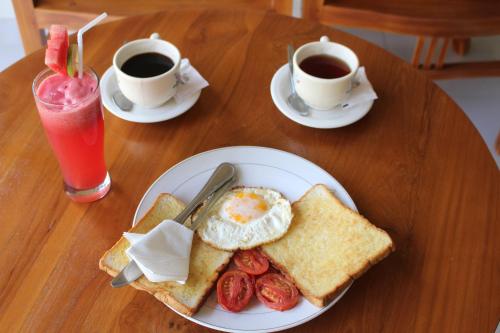a table with a plate of breakfast food and two cups of coffee at Magus Homestay in Pemuteran