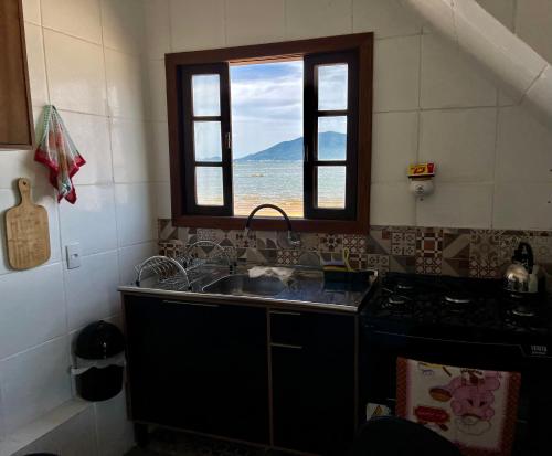 a kitchen with a sink and a window with a view of the ocean at Recanto Pé na Areia SC in Palhoça