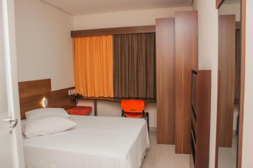 sypialnia z białym łóżkiem i pomarańczowym krzesłem w obiekcie Hotel e Pousada Bem Bom - Itu w mieście Itu
