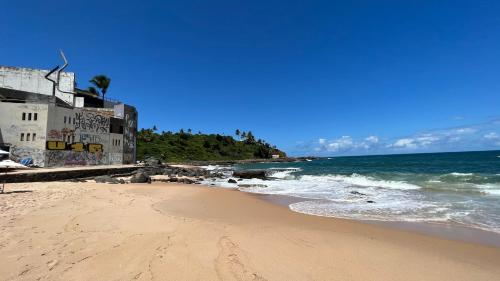 a sandy beach with a building and the ocean at Lindo vista mar na Praia do Buracão - Rio Vermelho in Salvador