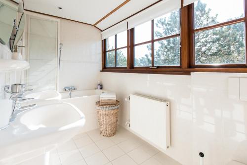 a white bathroom with two sinks and a tub and windows at Villa met grote tuin in de duinen nabij het strand in Buren