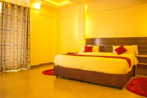 a bedroom with a large bed with yellow walls and red pillows at ROYAL ACACIA HOTEL ISIOLO in Tarbaj