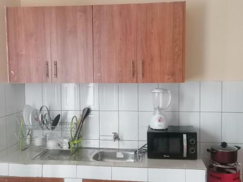 Kuchnia z drewnianymi szafkami, zlewem i kuchenką mikrofalową w obiekcie Nuri Homes w mieście Kisii