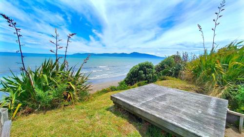 un banco de madera sentado en un lado de la playa en The Beach House Raumati, en Paraparaumu