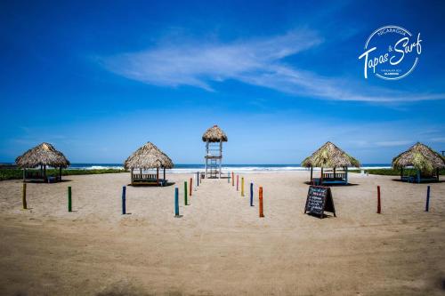 a beach with some straw umbrellas and signs in the sand at Tapas & Surf in Petacaltepe