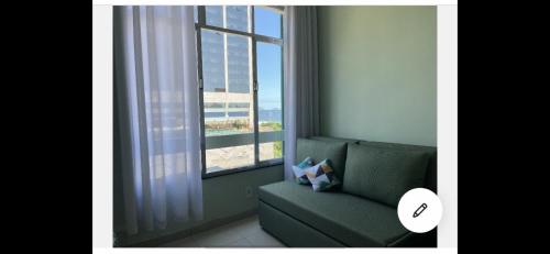 sala de estar con sofá verde y ventana en Studio com linda vista para a praia de Copacabana!, en Río de Janeiro