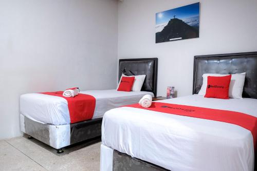 two beds with red and white sheets in a room at RedDoorz @ Cempaka Putih Jambi in Jambi