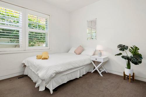 a white bedroom with a bed and a desk and windows at St Kilda Style - Stunning 3 Bedroom House in Melbourne