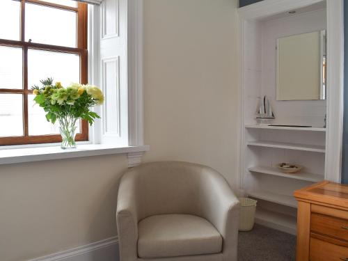 uma sala de estar com uma cadeira e um vaso de flores numa janela em Acarsaid Cottage em Portknockie
