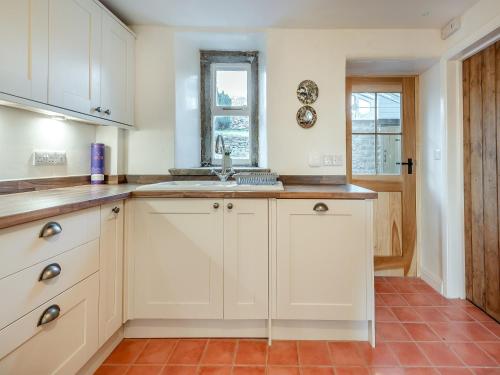 uma cozinha com armários brancos e um lavatório em Badger Cottage em Cressbrook