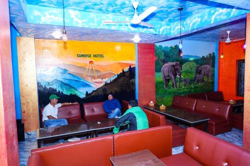 three men sitting in a restaurant with a mural on the wall at Sunrise Hotel in Bharatpur