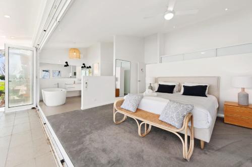 a white bedroom with a large bed and a bench at Ebb and Flow Sandy Point Road 70 in Corlette