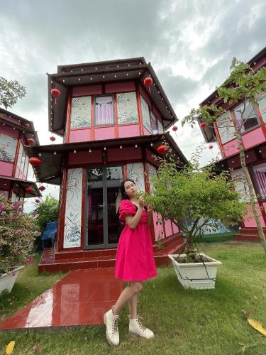 Una ragazza con un vestito rosa in piedi davanti a una casa di Homestay Pink House (Ngôi nhà màu hồng) a Ấp Ðông Qứi