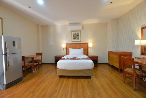 a bedroom with a bed and a desk and a refrigerator at Royal Suites Condotel in Kalibo