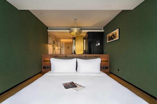 a bedroom with a large white bed with a green wall at S&N Yiting Hotel Taizhou in Taizhou