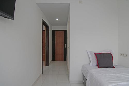 a white bedroom with two beds and a hallway at Hotel O Koala House in Pekanbaru