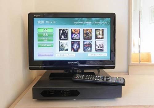 a computer monitor sitting on a stand with a remote control at Nest Hotel Matsuyama in Matsuyama