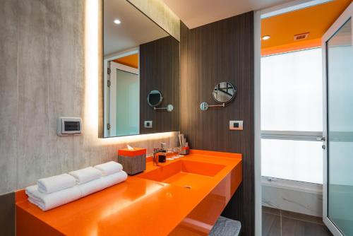 an orange bathroom with a sink and a mirror at Maitria Hotel Rama 9 Bangkok - A Chatrium Collection in Bangkok