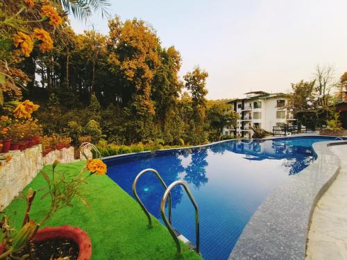 a large swimming pool with green grass and a building at Ataraxia Crestmont Resort & Spa in Dehradun