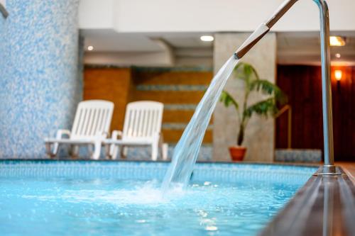 una fuente de agua en una piscina con sillas blancas en Aranyhomok Business-City-Wellness Hotel, en Kecskemét