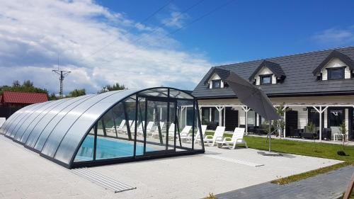 a glass pavilion with a swimming pool in front of a house at Osada Wypoczynku Jantar Resort&Spa - Luksusowe Domki z Basenem, Sauną i Jacuzzi in Jantar